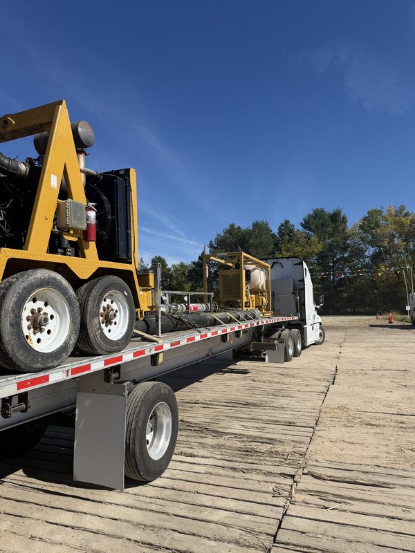 Najax flatbed hauling yellow trailer-mounted industrial pump units, chained down