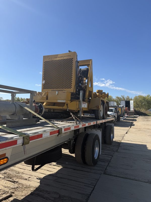 Yellow industrial pump unit secured with chains and straps on a flatbed trailer